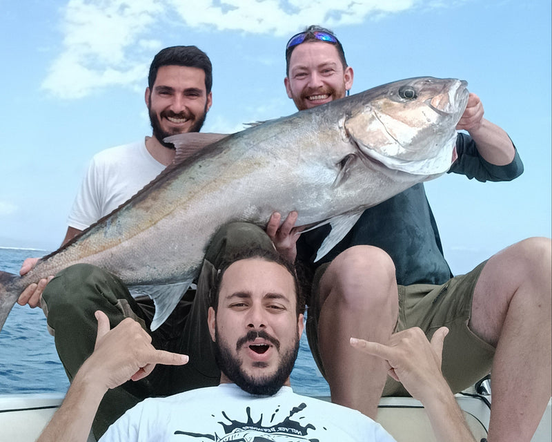 Three men on a boat holding a large fish with a clear blue sky in the background